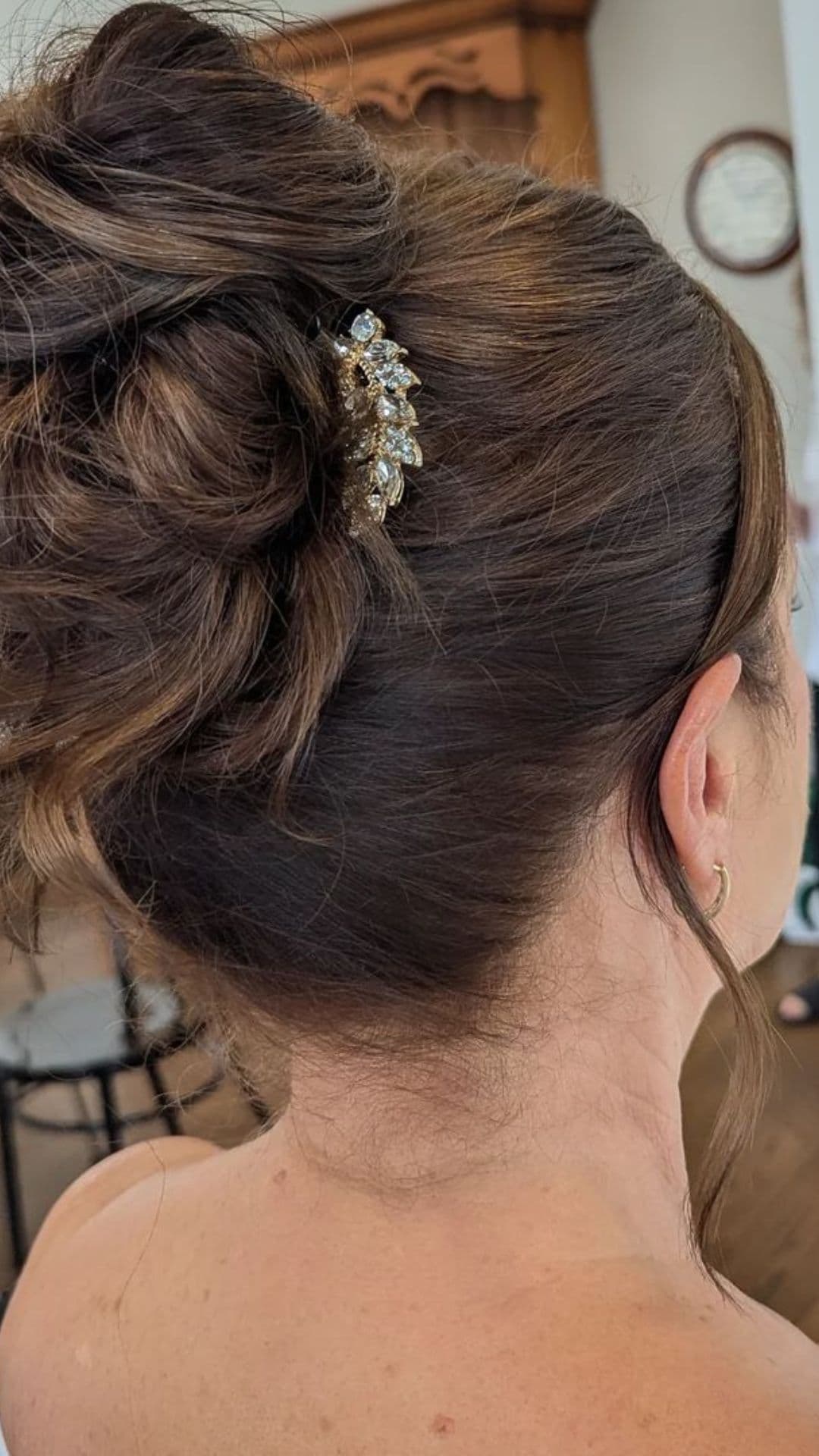 A woman with a messy bun hairstyle, featuring a decorative hairpiece, viewed from behind.