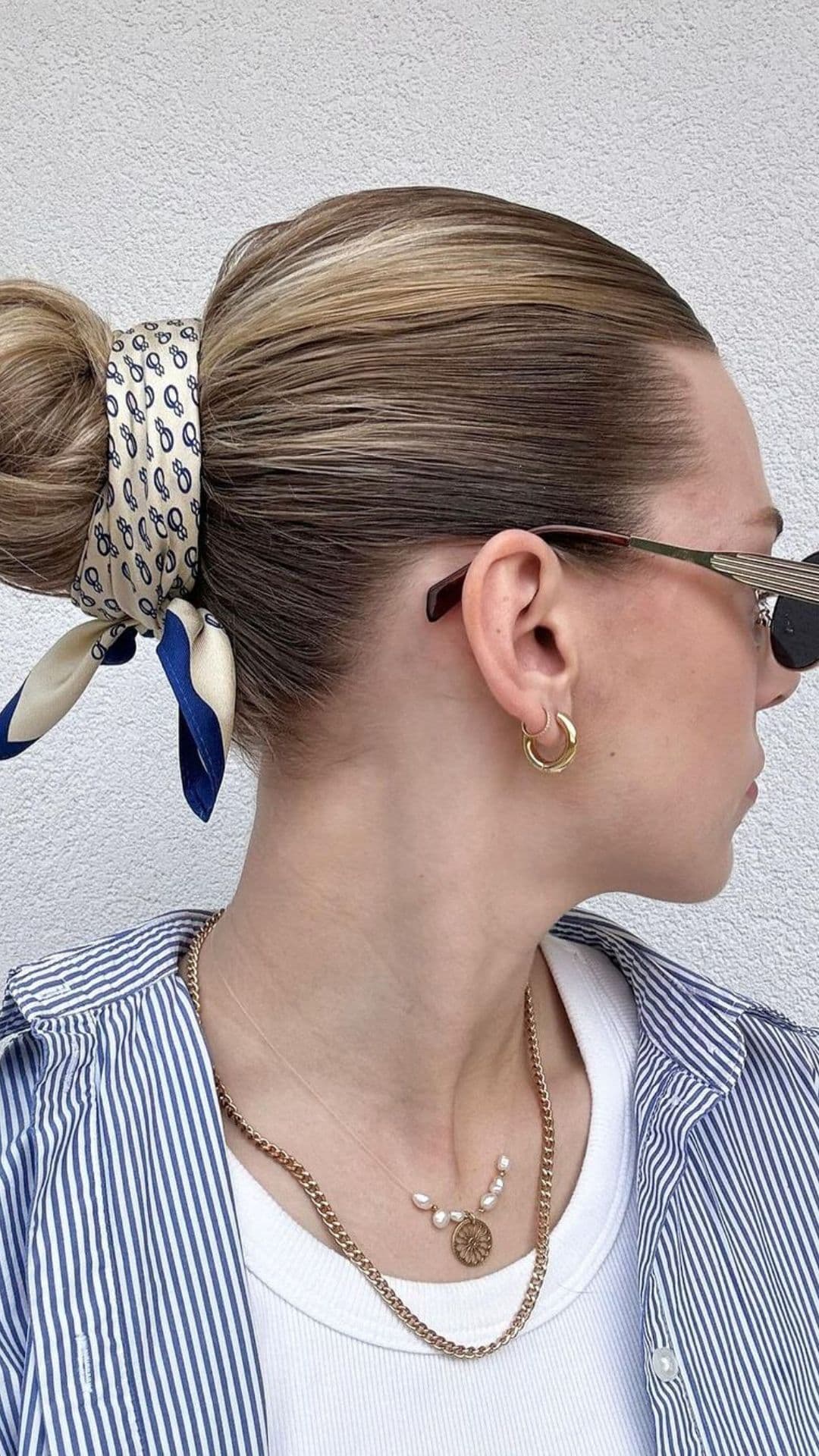 A person with a Scarf Bun hairstyle, wearing a striped shirt, sunglasses, and gold hoop earrings. The scarf is patterned with blue and white.