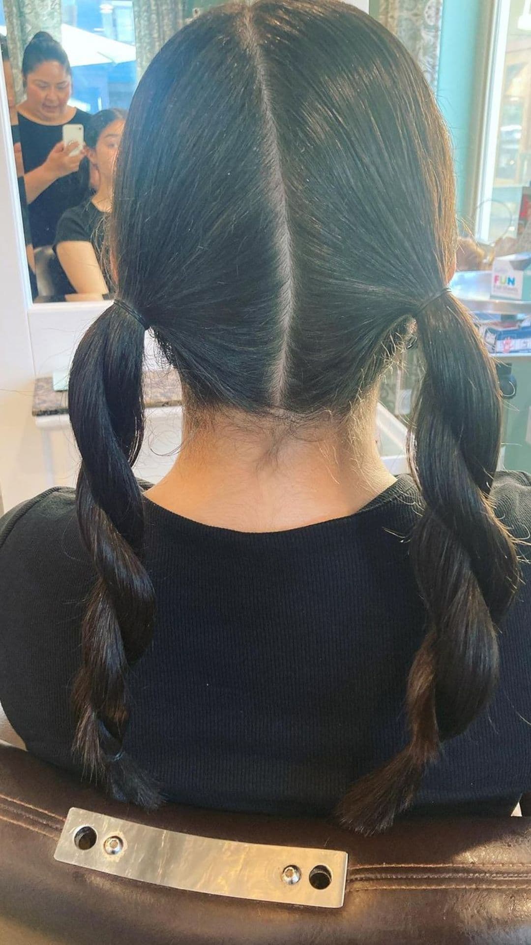 View of a person from behind showcasing Twisted Pigtails hairstyle in a salon setting. Their hair is divided in the middle, twisted into neat pigtails.