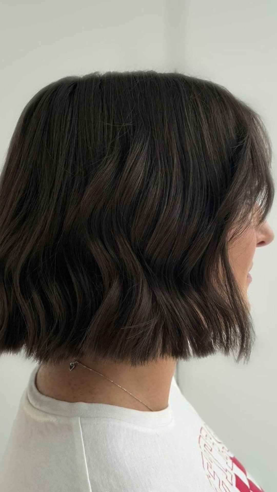 A person with a wavy bob hairstyle, showing the side view of their dark hair.