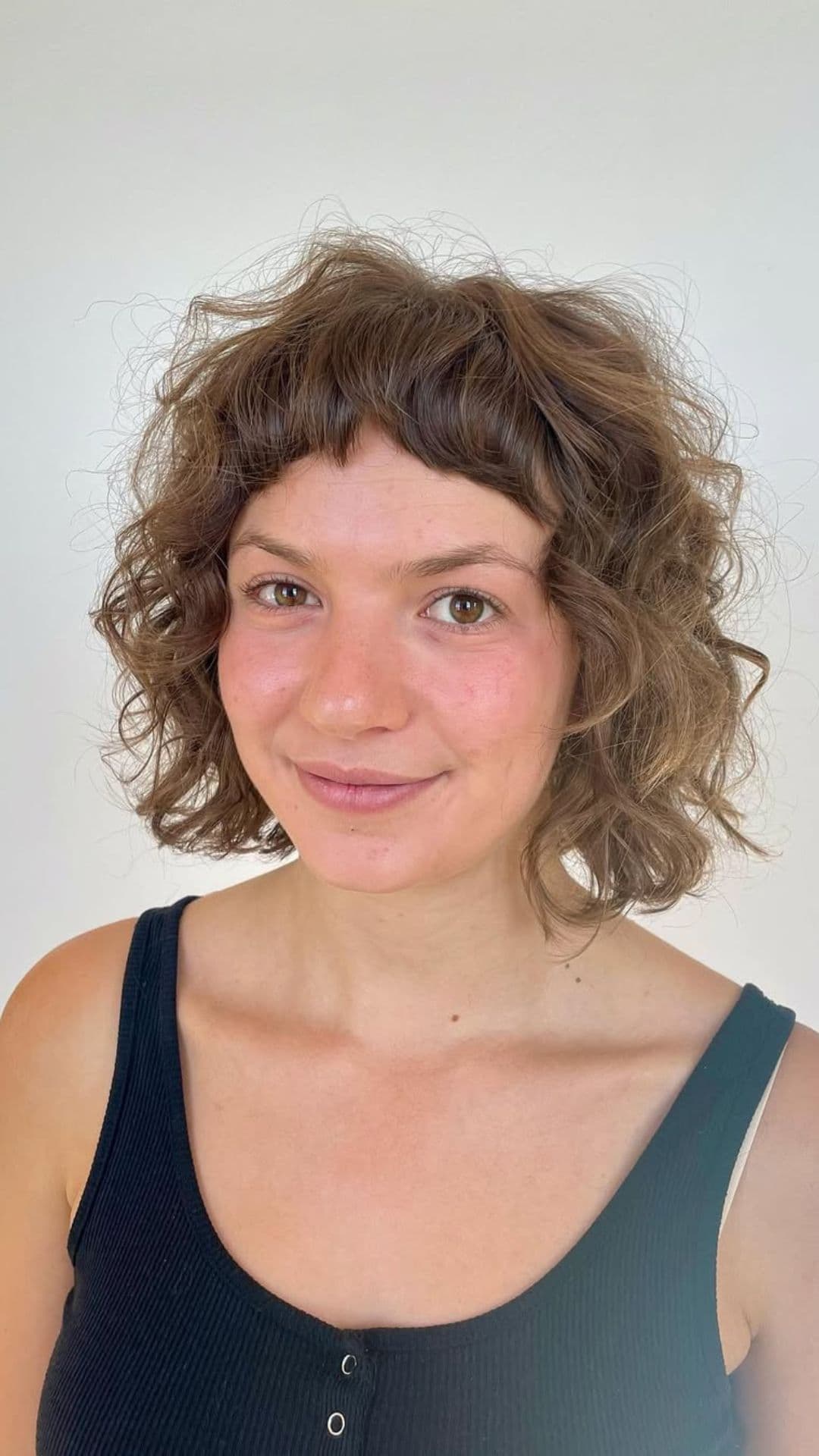 A woman with a round face modelling a Curly Bob hairstyle.